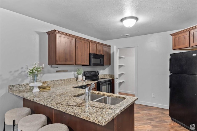 491 S Freedom Blvd Unit 104204, Provo, UT 84601 - kitchen with black appliances, a peninsula, a breakfast bar area, light stone countertops, and dark wood-style flooring