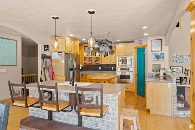 135 W Cove Dr, Elk Ridge, UT 84651 - kitchen featuring appliances with stainless steel finishes, arched walkways, a center island with sink, light wood-type flooring, and recessed lighting