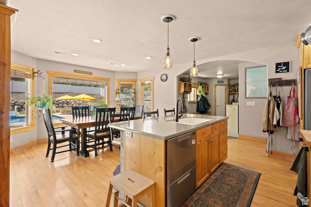 135 W Cove Dr, Elk Ridge, UT 84651 - kitchen with arched walkways, stainless steel dishwasher, light wood-style floors, hanging light fixtures, and a center island with sink