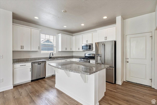5239 W Mellow Way S, Jordan, UT 84009 - kitchen featuring appliances with stainless steel finishes, a center island, wood finished floors, white cabinets, and a textured ceiling
