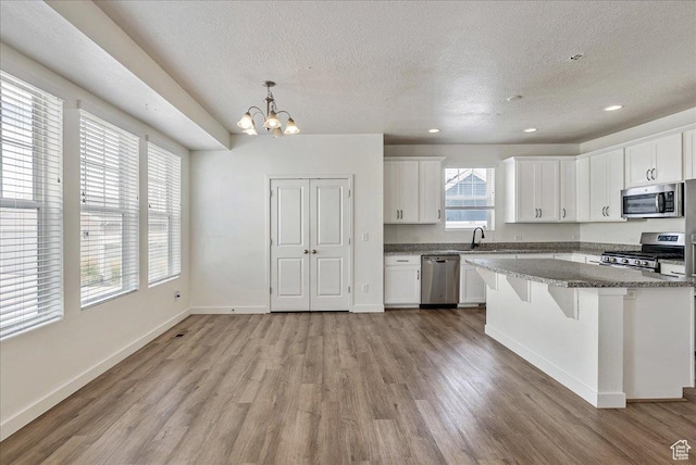 5239 W Mellow Way S, Jordan, UT 84009 - kitchen featuring stainless steel appliances, a textured ceiling, light wood finished floors, a chandelier, and white cabinetry
