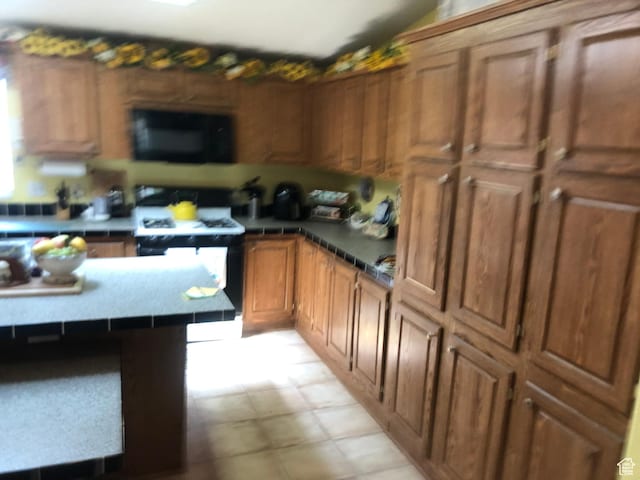 15700 N 7100 E, Spring City, UT 84662 - kitchen with black microwave, range, brown cabinetry, and tile countertops