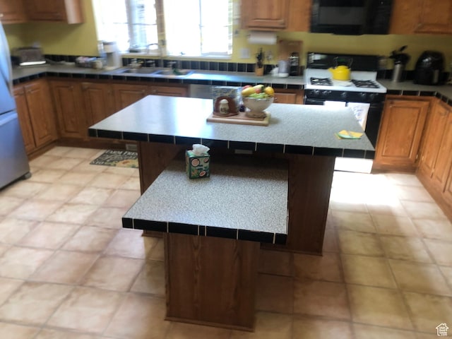15700 N 7100 E, Spring City, UT 84662 - kitchen with black range with gas stovetop, a kitchen island, freestanding refrigerator, brown cabinets, and tile counters