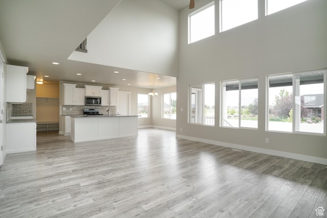 3045 S 2275 W, West Haven, UT 84401 - unfurnished living room featuring healthy amount of natural light, light wood finished floors, a chandelier, a towering ceiling, and recessed lighting