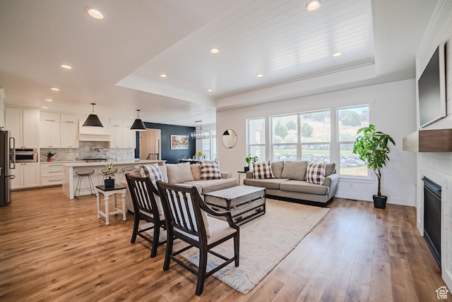 3698 E Butterfield Rd, Eagle Mountain, UT 84005 - living room with a raised ceiling, a fireplace, light wood-style floors, a chandelier, and recessed lighting