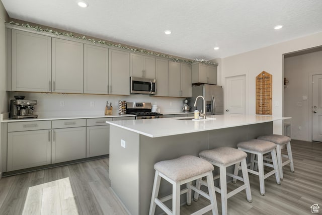 537 W Flora Dr, Saratoga Springs, UT 84045 - kitchen featuring stainless steel appliances, gray cabinets, light wood-type flooring, a kitchen bar, and a kitchen island with sink