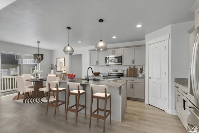 4273 W Watchmen Way, Herriman, UT 84096 - kitchen featuring appliances with stainless steel finishes, decorative backsplash, light wood-style floors, a breakfast bar, and an island with sink