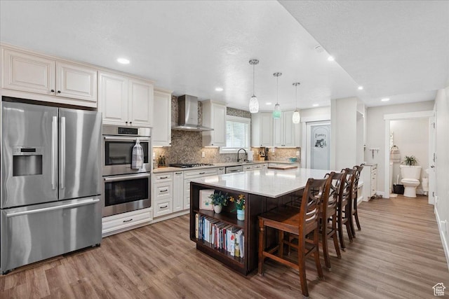 5719 W Boulder Creek Rd, West Jordan, UT 84081 - kitchen featuring appliances with stainless steel finishes, wall chimney range hood, light wood-style floors, tasteful backsplash, and a kitchen bar