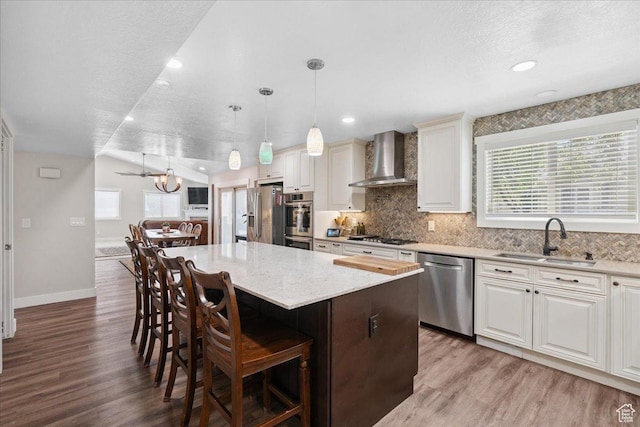 5719 W Boulder Creek Rd, West Jordan, UT 84081 - kitchen with appliances with stainless steel finishes, wall chimney exhaust hood, a kitchen island, a kitchen breakfast bar, and light wood finished floors