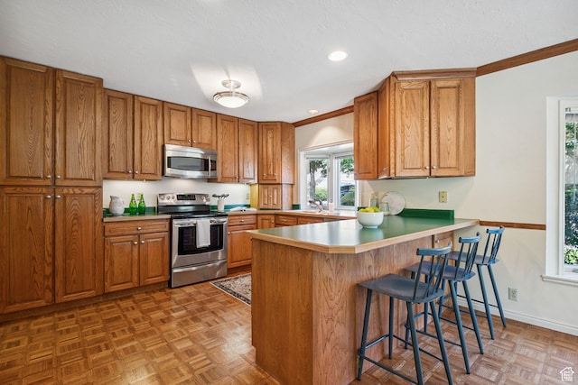 2056 E Sierra View Cir, Millcreek, UT 84109 - kitchen with stainless steel appliances, brown cabinets, a peninsula, a breakfast bar area, and crown molding