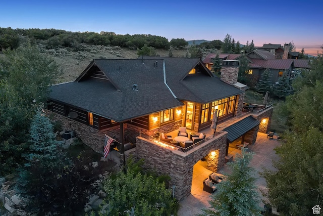 9388 Dye Cabins Dr, Park City, UT 84098 - back of property at dusk featuring stone siding, roof with shingles, a chimney, and a patio area