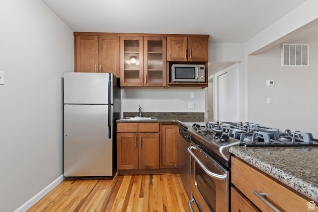 650 N 300 W Unit 229, Salt Lake City, UT 84103 - kitchen with stainless steel appliances, brown cabinetry, light wood-style flooring, dark stone countertops, and glass insert cabinets