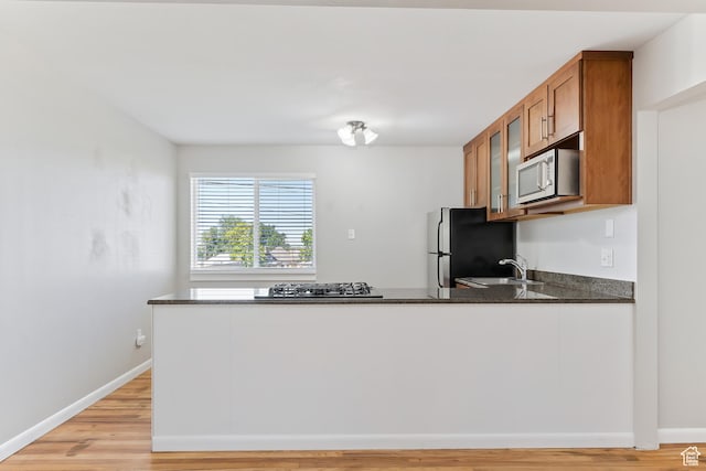 650 N 300 W Unit 229, Salt Lake City, UT 84103 - kitchen featuring stainless steel appliances, brown cabinetry, a peninsula, dark stone counters, and light wood-style flooring
