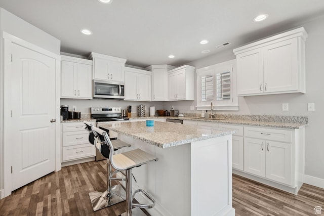 9634 N Red Bridge Rd, Eagle Mountain, UT 84005 - kitchen featuring stainless steel appliances, wood finished floors, white cabinetry, a kitchen island, and a breakfast bar