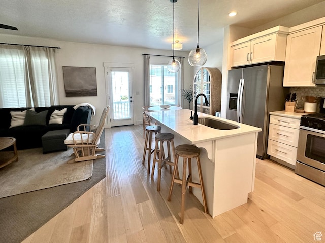 214 W Whitewater Dr, Vineyard, UT 84059 - kitchen featuring appliances with stainless steel finishes, light wood-style floors, a kitchen bar, a kitchen island with sink, and light countertops