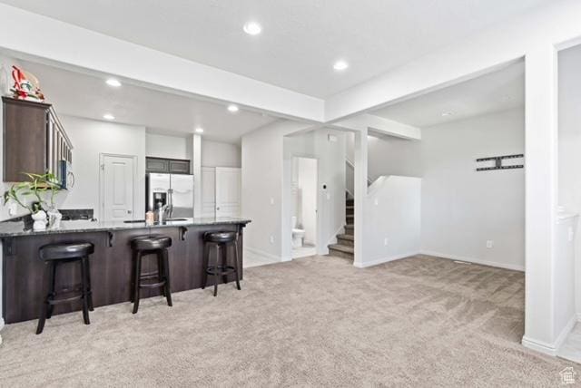 3057 S Finsbury Ln, West Valley City, UT 84120 - kitchen with light carpet, a peninsula, a kitchen bar, stainless steel fridge, and dark brown cabinets