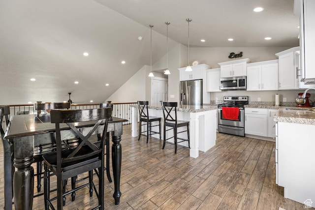 3973 E Eagle Top Ct, Eagle Mountain, UT 84005 - kitchen featuring appliances with stainless steel finishes, a kitchen island, wood finished floors, a kitchen breakfast bar, and white cabinetry
