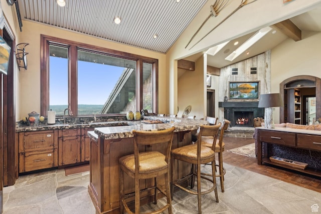10399 Summit View Dr N, Park City, UT 84060 - kitchen featuring beamed ceiling, dark stone counters, a kitchen breakfast bar, brown cabinetry, and a fireplace