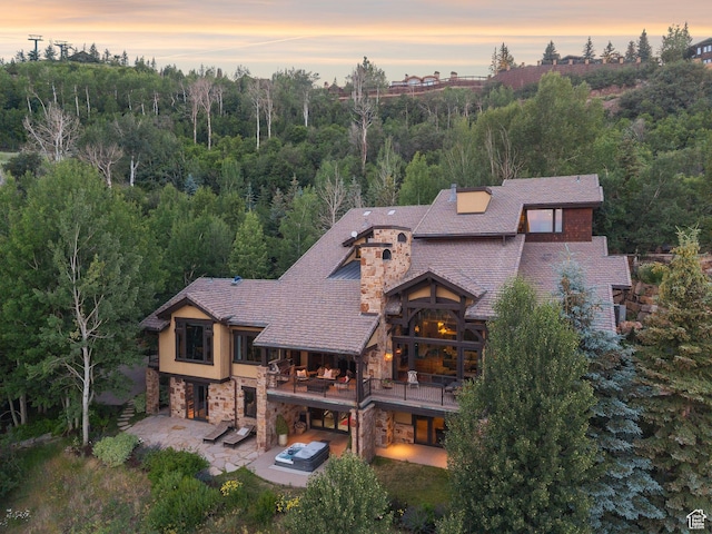 10399 Summit View Dr N, Park City, UT 84060 - back of house at dusk featuring a balcony, a patio, stone siding, and a forest view