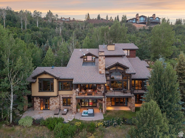 10399 Summit View Dr N, Park City, UT 84060 - back of property at dusk with a patio area, a balcony, stone siding, french doors, and an outdoor hot tub