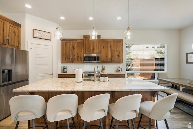 5336 W 3180 S, Hurricane, UT 84737 - kitchen featuring stainless steel appliances, decorative backsplash, light stone countertops, brown cabinets, and a kitchen bar