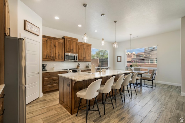 5336 W 3180 S, Hurricane, UT 84737 - kitchen with stainless steel appliances, an island with sink, light wood-type flooring, tasteful backsplash, and a kitchen breakfast bar
