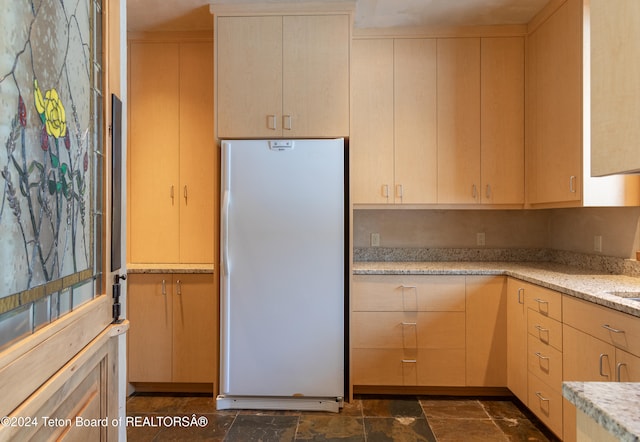 kitchen with light stone countertops, light brown cabinets, and white fridge