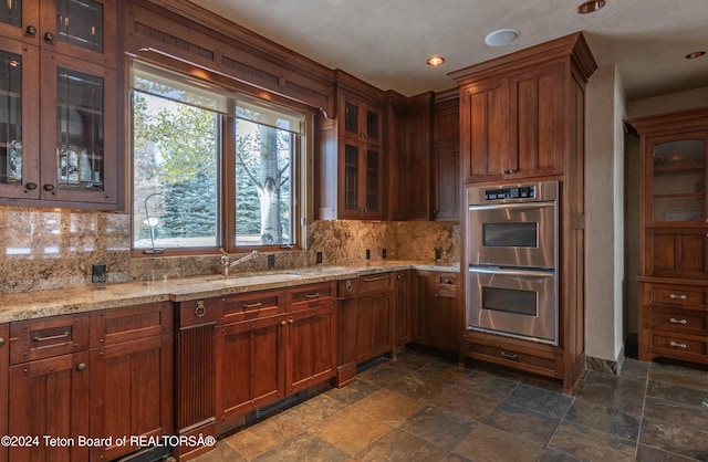 kitchen with decorative backsplash, sink, stainless steel double oven, and light stone counters