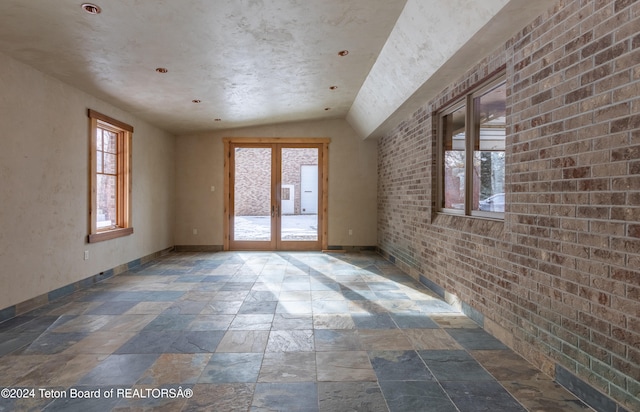 empty room featuring french doors, brick wall, and vaulted ceiling