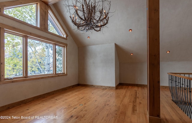 additional living space featuring a notable chandelier, vaulted ceiling with beams, plenty of natural light, and light hardwood / wood-style flooring