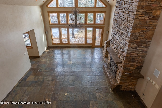 unfurnished living room featuring a healthy amount of sunlight, a stone fireplace, high vaulted ceiling, and an inviting chandelier