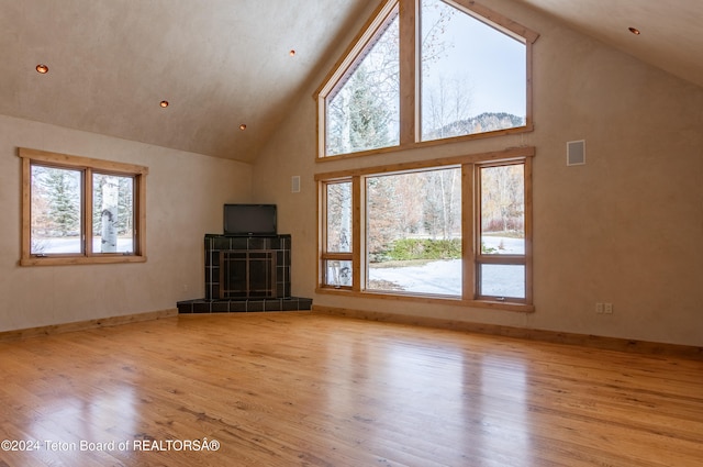 unfurnished living room with a tiled fireplace, high vaulted ceiling, and light hardwood / wood-style floors