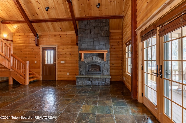 unfurnished living room with french doors, wooden ceiling, vaulted ceiling with beams, a stone fireplace, and wood walls