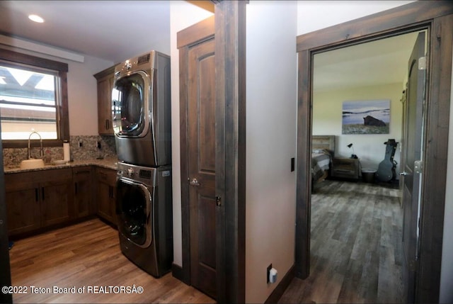 clothes washing area with stacked washer / dryer, hardwood / wood-style floors, and sink