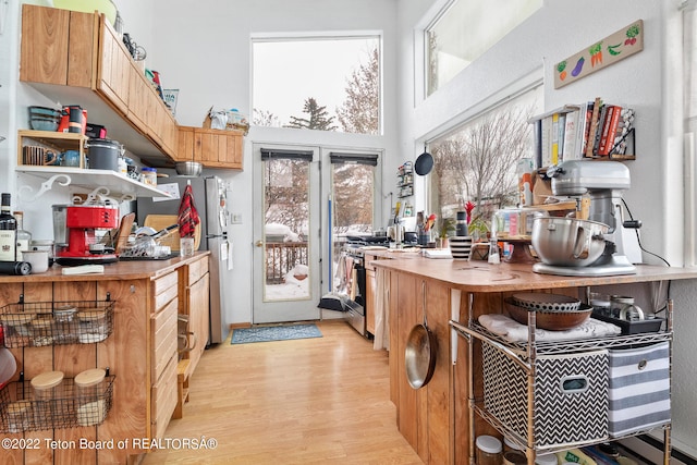 kitchen featuring a baseboard heating unit, appliances with stainless steel finishes, light wood-type flooring, and a high ceiling