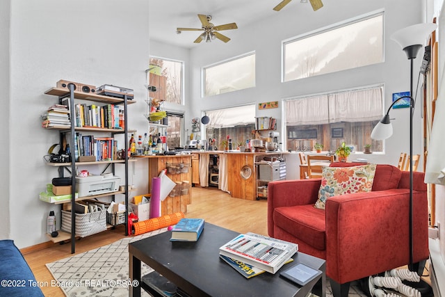 living room featuring a high ceiling, light hardwood / wood-style floors, and ceiling fan