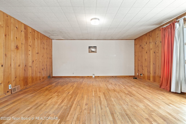 unfurnished room featuring light wood-type flooring and wood walls