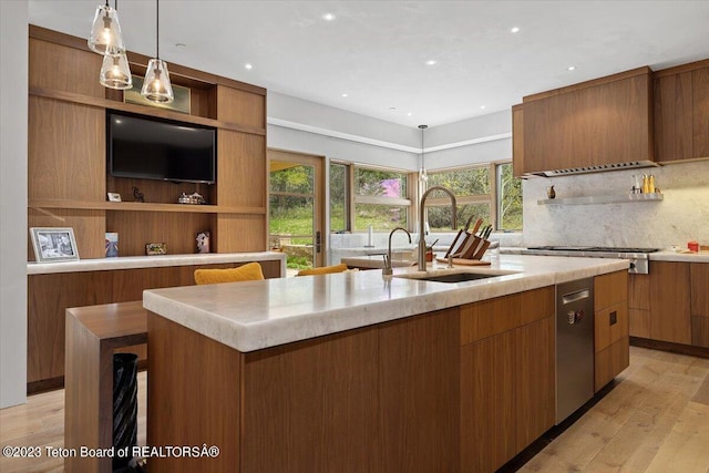 kitchen with a breakfast bar area, light hardwood / wood-style floors, a center island with sink, tasteful backsplash, and decorative light fixtures