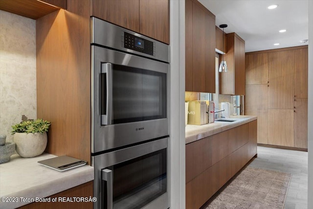 kitchen featuring decorative light fixtures, light hardwood / wood-style floors, double oven, and sink