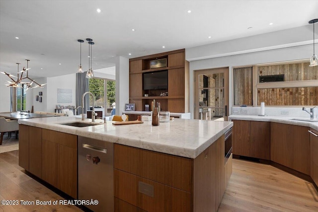 kitchen featuring light stone countertops, light hardwood / wood-style floors, sink, a center island with sink, and pendant lighting