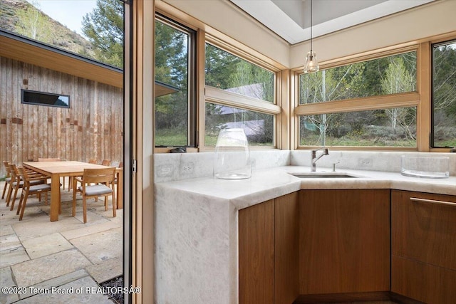 kitchen featuring wooden walls, sink, hanging light fixtures, and light tile floors