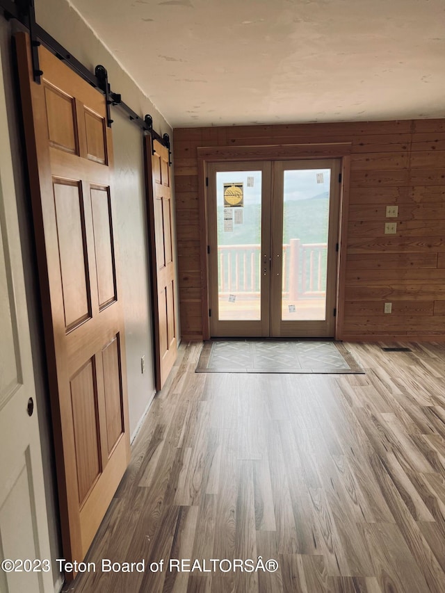 interior space with a barn door, wood walls, french doors, and light wood-type flooring