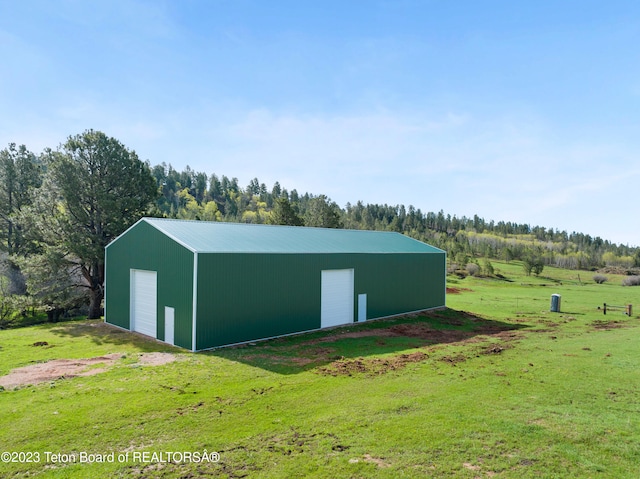 view of outdoor structure featuring a rural view, a lawn, and a garage