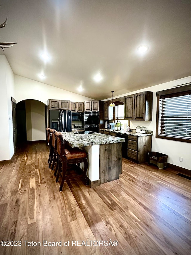 kitchen with pendant lighting, light hardwood / wood-style floors, vaulted ceiling, a kitchen bar, and a center island