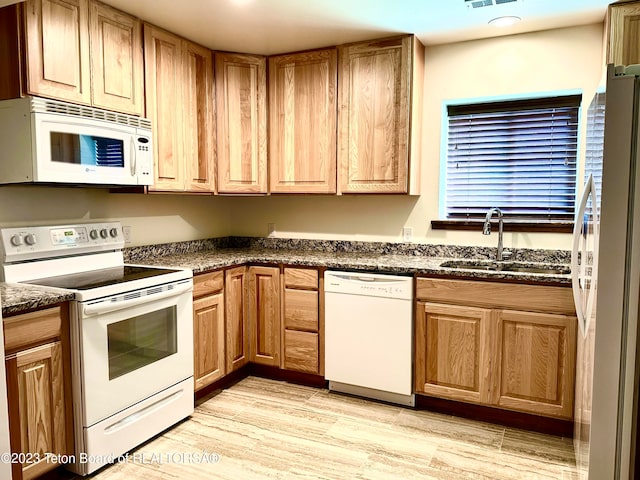 kitchen featuring light hardwood / wood-style flooring, white appliances, dark stone countertops, and sink