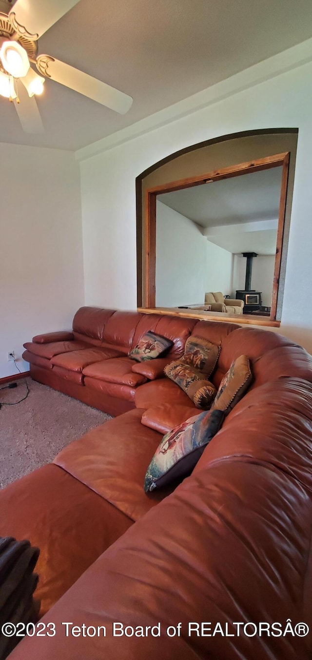 living room featuring ceiling fan, a wood stove, and carpet floors