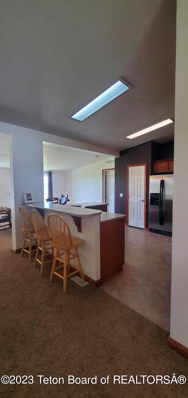 kitchen featuring a skylight, dark colored carpet, stainless steel fridge, and a breakfast bar area