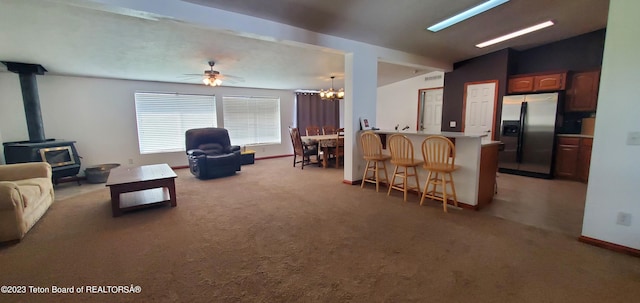 living room featuring a wood stove, carpet floors, vaulted ceiling, and ceiling fan with notable chandelier