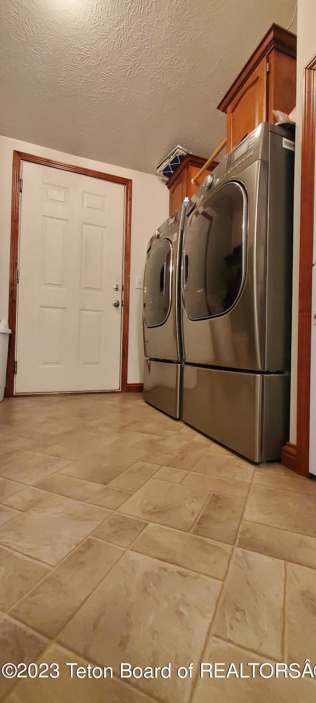 laundry room featuring a textured ceiling, washing machine and dryer, light tile floors, and cabinets