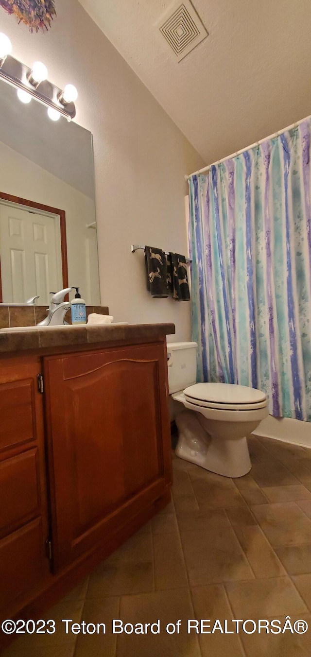 bathroom featuring lofted ceiling, tile floors, toilet, and vanity